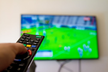 Close-up macro of man's hand with TV remote control watching a rugby match