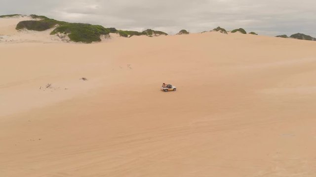 Whte and Orange buggy car driving on sand dunes in a cloudy day in Natal, Brazil