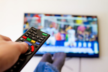 Close-up macro of man's hand with TV remote control watching a soccer match