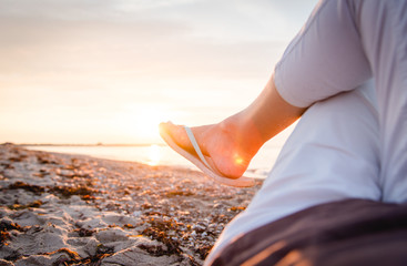 Relaxed feet on the beach with sandals in the evening sun in the back light with anklets and flip flops