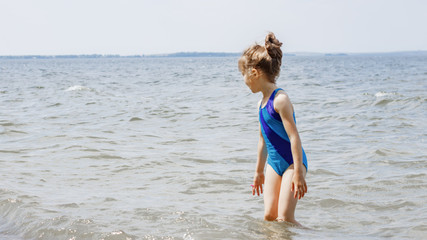 a girl in a blue swimsuit walks along the seashore