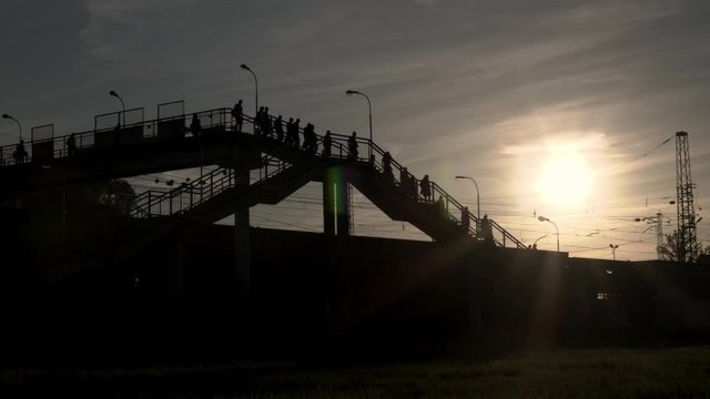 Силуэты людей на фоне солнца идут по мосту.
