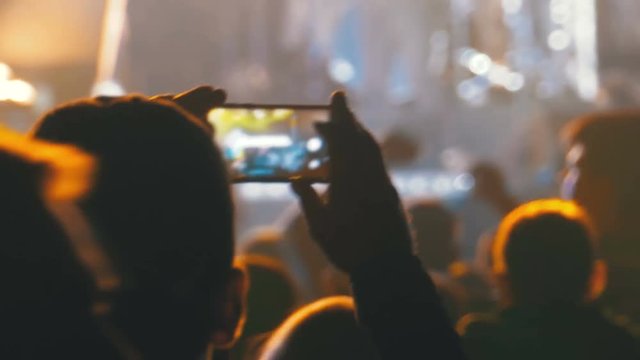 People at Music Rock Concert Taking Photos or Recording Video with Smartphones. Fan person filming on mobile smart phone at concert party crowd cheering at rock music event with flashing light show