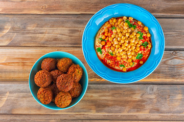 Falafel balls in a dish and hummus, chickpea, tahini with olive oil, pepper, spices in a plate on wood background. Traditional Middle Eastern healthy vegan food.