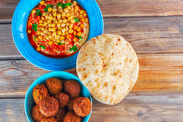 Falafel balls in a dish, pita bread and hummus, chickpea, tahini with olive oil, pepper, spices in a plate on wood background. Traditional Middle Eastern healthy vegan food.Flat lay, top view.