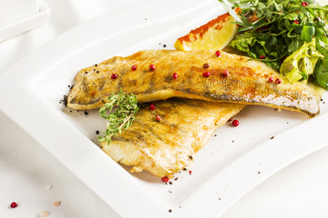 Baked fish fillet with lemon and fresh vegetables on white plate