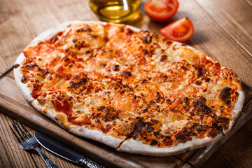 Pizza with tomatoes and cheese on wooden rustic table.