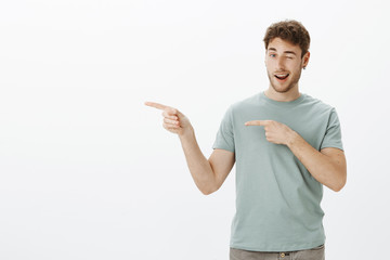 You would not regret if visit that place. Charming flirty mature guy in t-shirt, pointing left with index fingers, sticking out tongue and winking, flirting while talking with gorgeous woman