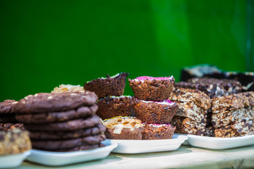 Homemade vegan chocolate snacks with dried raspberry, grated coconut, nuts, cocoa on a wooden board with green background