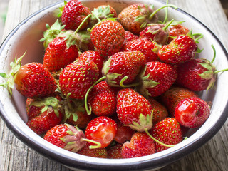 Ripe red strawberries in white old dish on wooden table