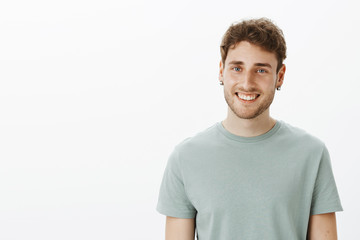 Obraz premium Portrait of satisfied happy Caucasian man in earrings and t-shirt, smiling broadly and gazing pleased at camera, talking casually with good friend, enjoying spending time with close people