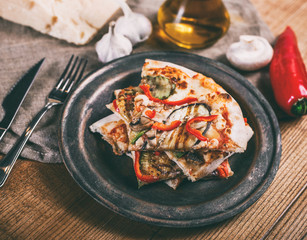 Sliced pizza with chicken, zucchini, eggplant, pepper, cheese and mushrooms on the plate vintage. Top view. Toning.
