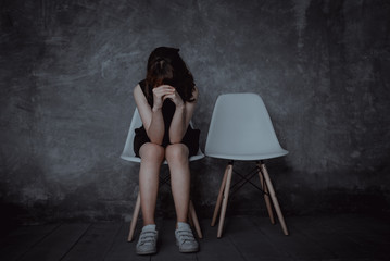 Sad woman with depression and lonely mood sitting alone in empty room.