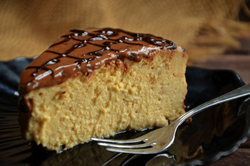 A piece of cheesecake covered with caramel on a black plate