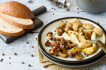 Fried mushrooms chanterelles and young potatoes on a round plate on an old wooden table.