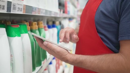 Salesperson hands using pc tablet in front of cleaners shelves in modern grocery retail store - Powered by Adobe