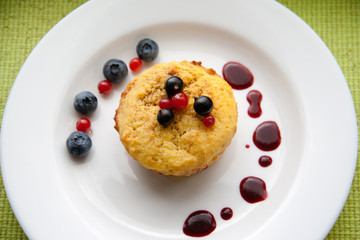 Homemade black currant cheese muffin with fresh berries and cherry sauce on white plate