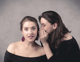 Two fancy dressed actress girls with long hair and make up whispering in front of grey urban background concept.