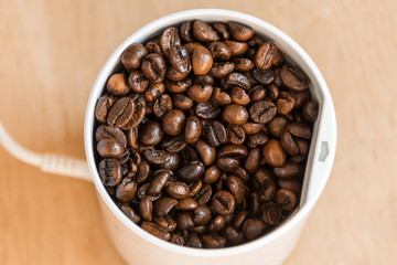 Coffee beans in a modern coffee grinder closeup on wooden background. Roasted aromatic coffee top view.