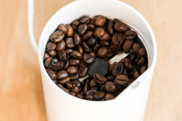 Coffee beans in a modern coffee grinder closeup on wooden background. Roasted aromatic coffee top view.