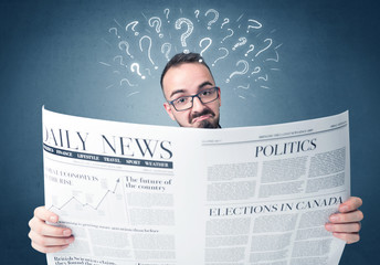 Young confused businessman reading daily newspaper with question marks above his head