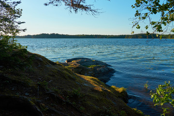 Coast of the lake on a sunset. Blue water and stones on sunshine. 