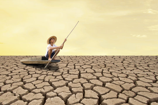 Climate change and Drought impact. Young man sitting on wooden boat at dry land.