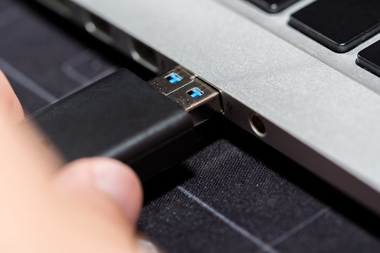 Hand inserting USB flash memory drive plugged into a computer laptop port.
