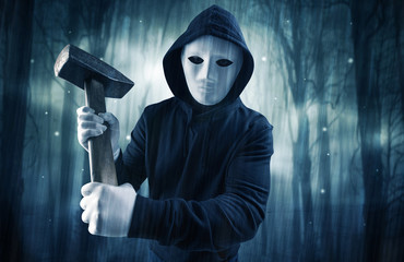 Masked armed hitman in dark thick forest with foggy mysterious concept
