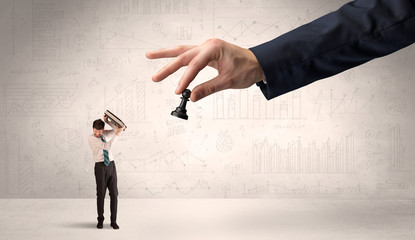 Little businessman is afraid to make the next step in his chess game with graphs, charts and...