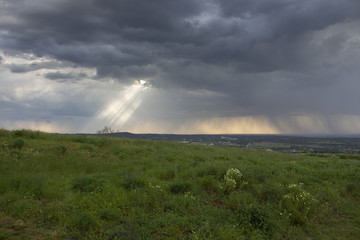 Naklejka na ściany i meble Sunlight coming through clouds during a storm on a beautiful grassland area