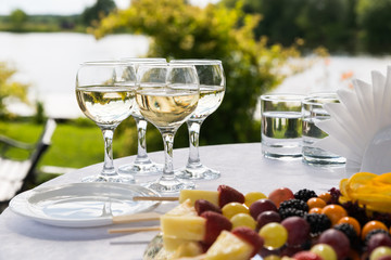 Round white table with glasses of champagne and the mirror dish with a fruit skewer on the nature