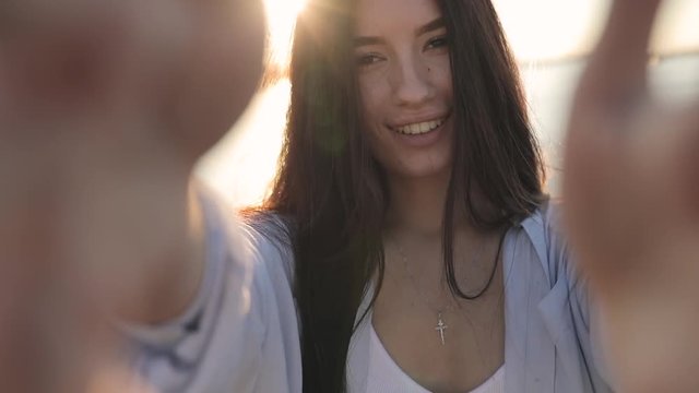 Young smiling woman holding camera make selfie video in sun beams, slow motion