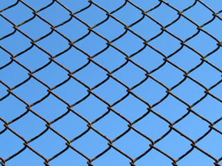 Wire mesh isolated on blue sky background. Rusty wired fence, metallic net