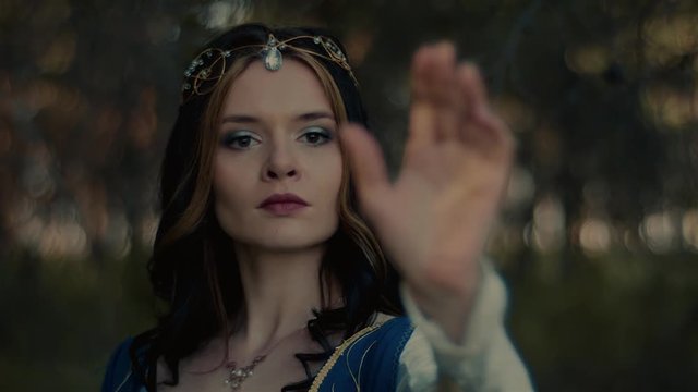 Close up portrait of charming brunette magician summoning wood spirit. Gorgeous elf woman spends time in the forest.