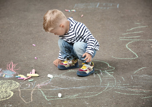 Cute little boy drawing with chalk on  asphalt