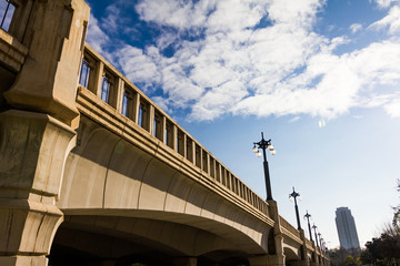 Fototapeta premium Bright blue spring sky with white clouds and concrete bridge with street lamps at public park in Valencia, Spain
