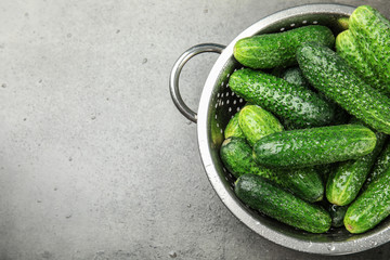 Colander with ripe fresh cucumbers on table, top view
