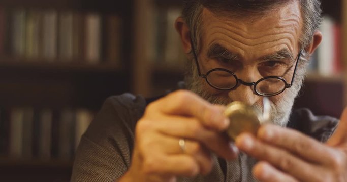 Close Up Of The Pld Man With Gray Hair And In Glasses Opening Watch On The Chain, Looking At It And Putting Away. At The Library.