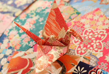 Close up of a colorful Japanese origami paper crane on a stack of patterned, colorful papers