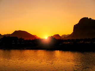 Naklejka na ściany i meble Sunset over Nam Song River with silhouetted rock formations in Vang Vieng, Laos