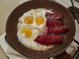 Appetizing smoked sausages and eggs for breakfast are fried in a frying pan in oil
