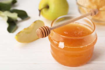 Jar of honey, apples and dipper on wooden table