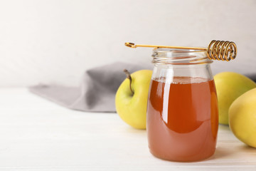 Jar of honey, apples and dipper on wooden table