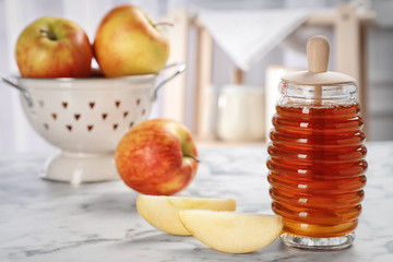Jar of honey with tasty apples on marble table