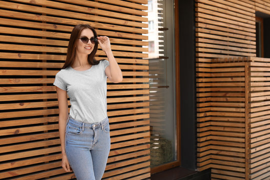 Young woman wearing gray t-shirt near wooden wall on street. Urban style