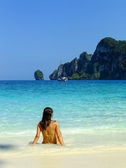 Young woman in bikini sitting at Ao Yongkasem beach on Phi Phi Don Island, Krabi Province, Thailand