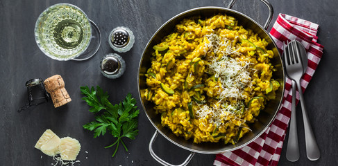 banner of Italian dish yellow Risotto milanese with saffron, zucchini and Parmesan cheese on a black slate table with white wine in a glass. north Italy kitchen