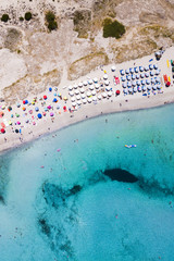 Aerial view of an emerald and transparent Mediterranean sea with a white beach full of beach umbrellas and tourists who relax and take a bath. Costa Smeralda, Sardinia, Italy.
