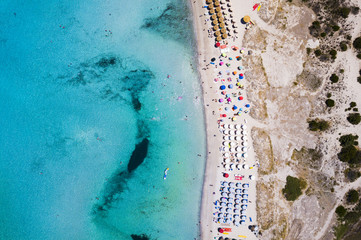 Aerial view of an emerald and transparent Mediterranean sea with a white beach full of beach umbrellas and tourists who relax and take a bath.Sardinia, Italy.